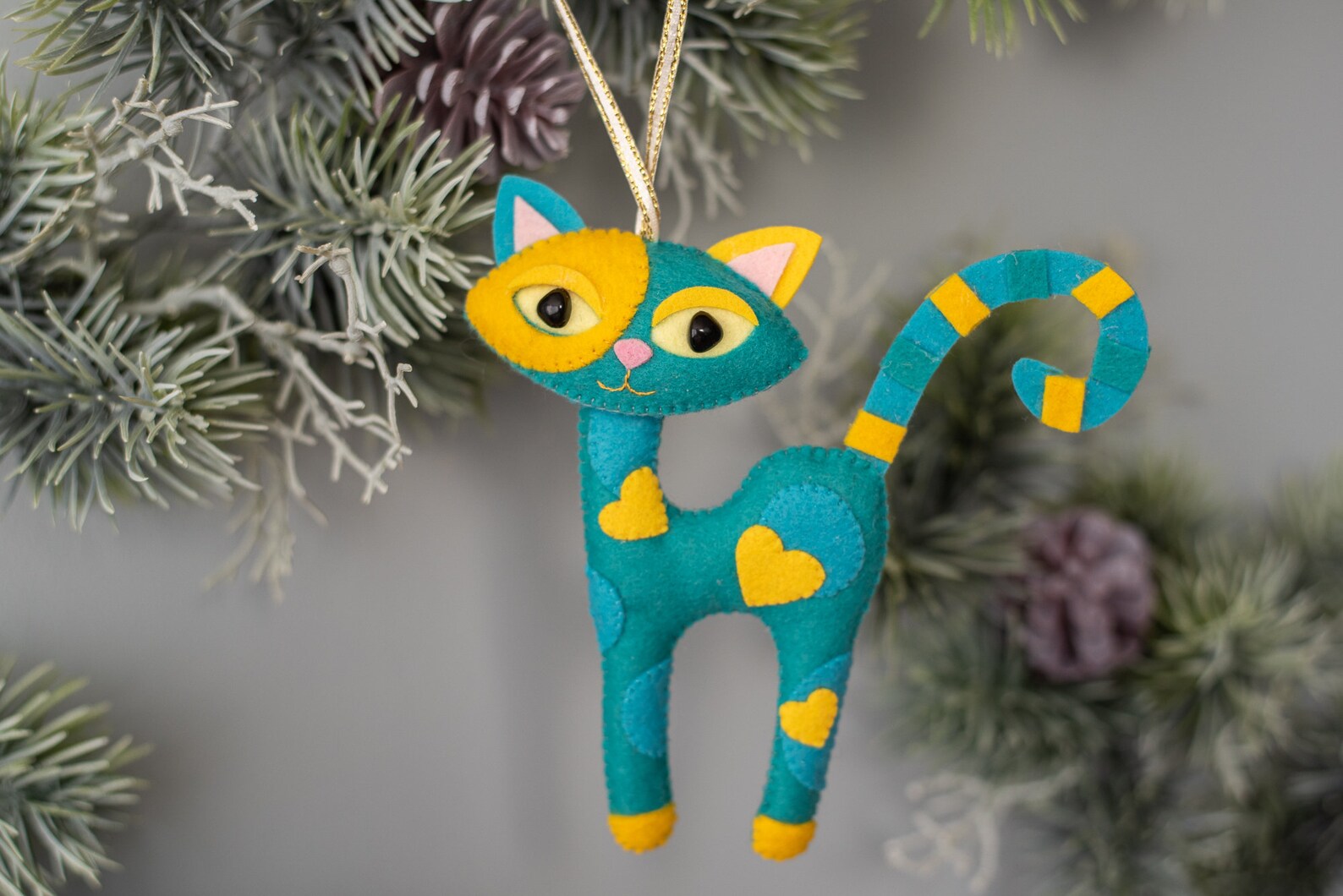 A handcrafted green felt cat with white yellow hearts. The cat has large yellow eyes, long paws and tail.
