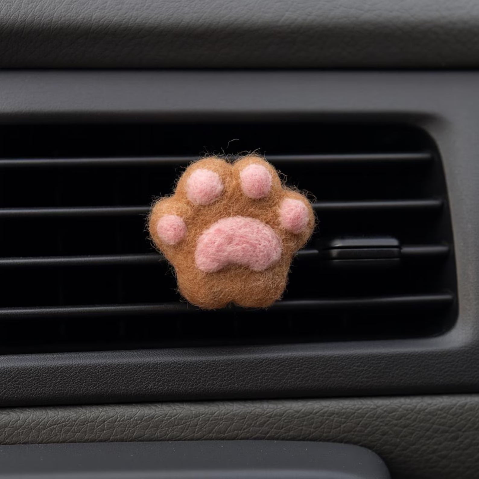 A soft brown felt cat paw with pink pads for attached to a car air vent as a cute decorative clip or nature air freshener.
