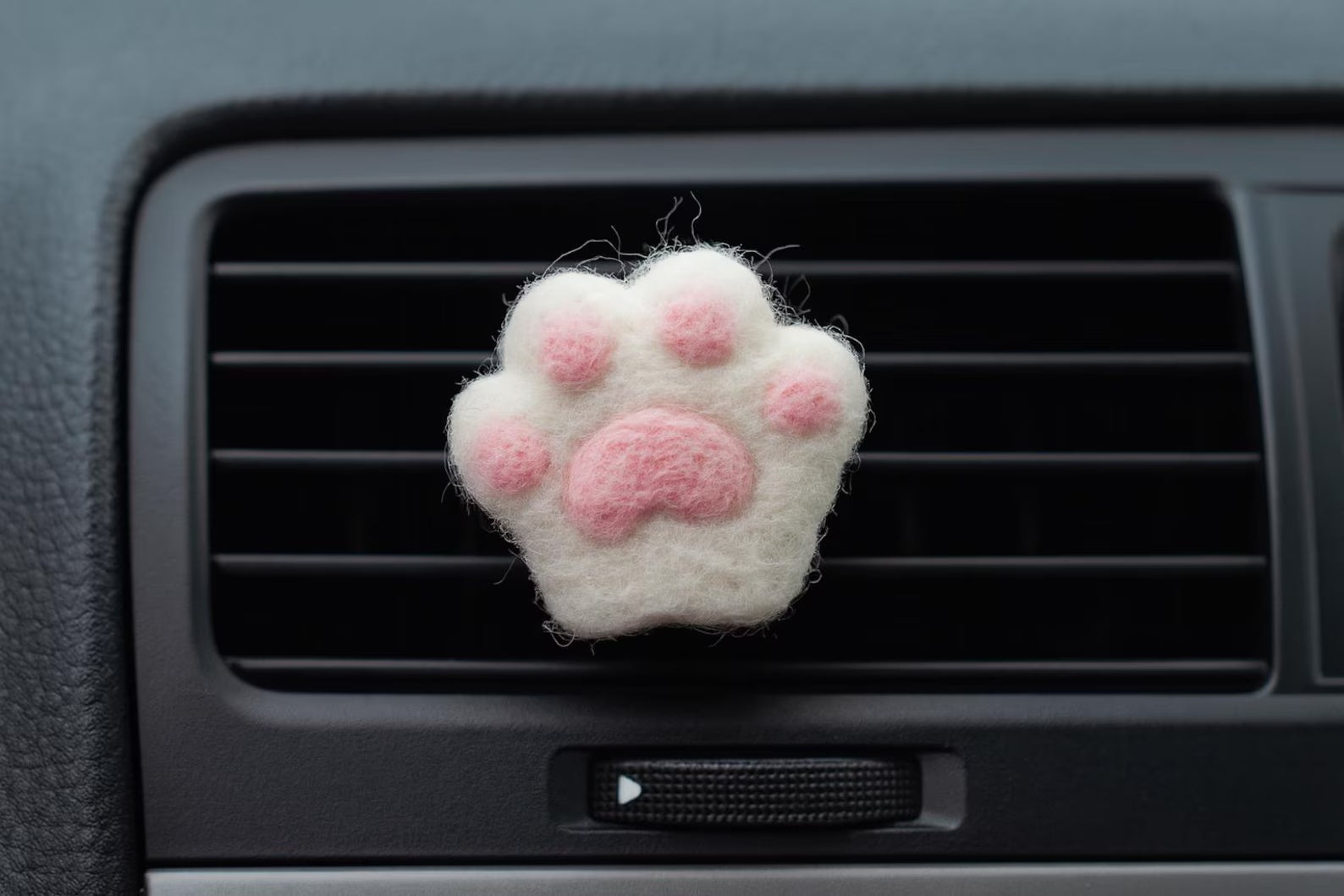 A soft white felt cat paw with pink pads for attached to a car air vent as a cute decorative clip or nature air freshener.