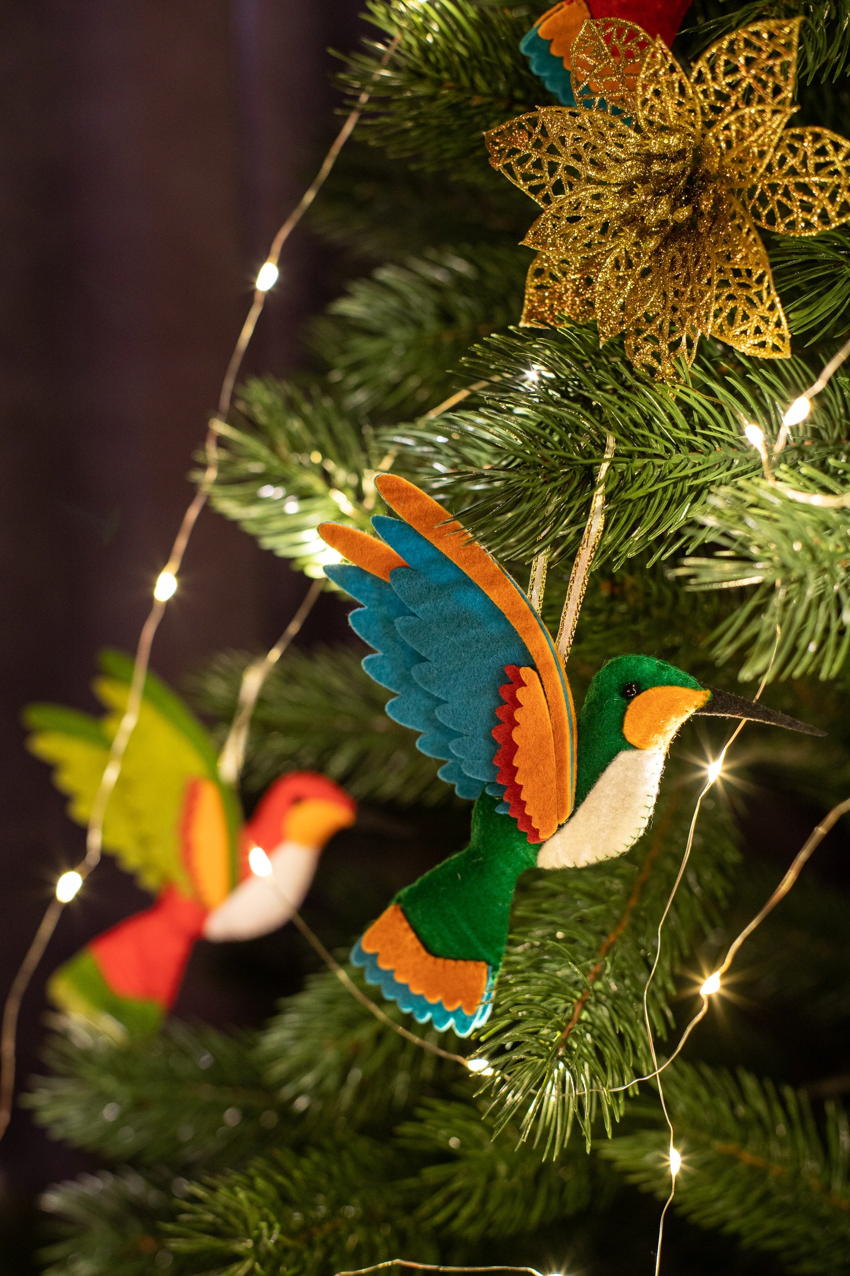A handmade green felt hummingbird ornament with a white belly, blue wings, and a black beak