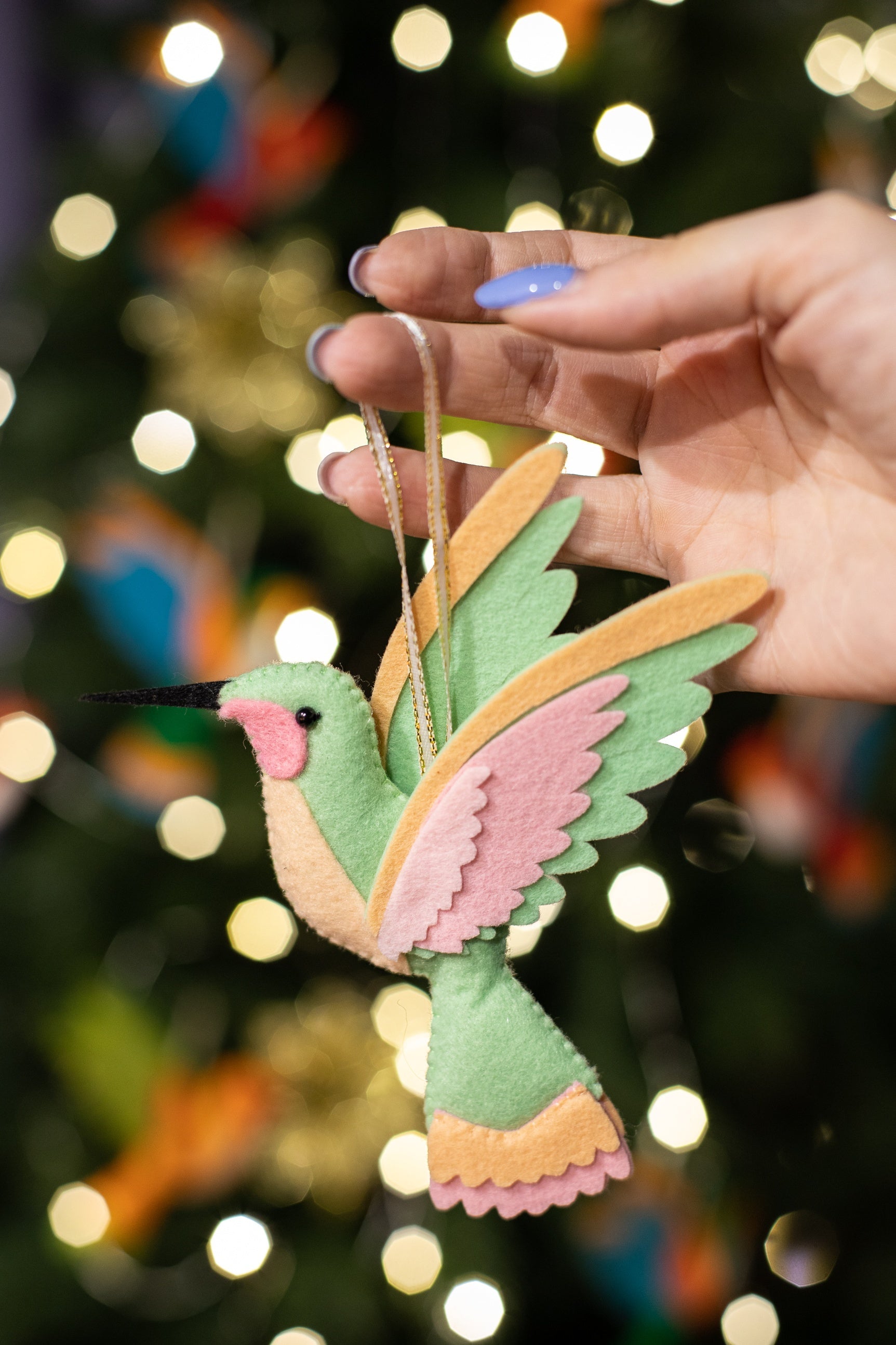 Handmade felt hummingbird ornament. The bird is mint green with a black beak. Its wings are a blend of peach and light pink. 