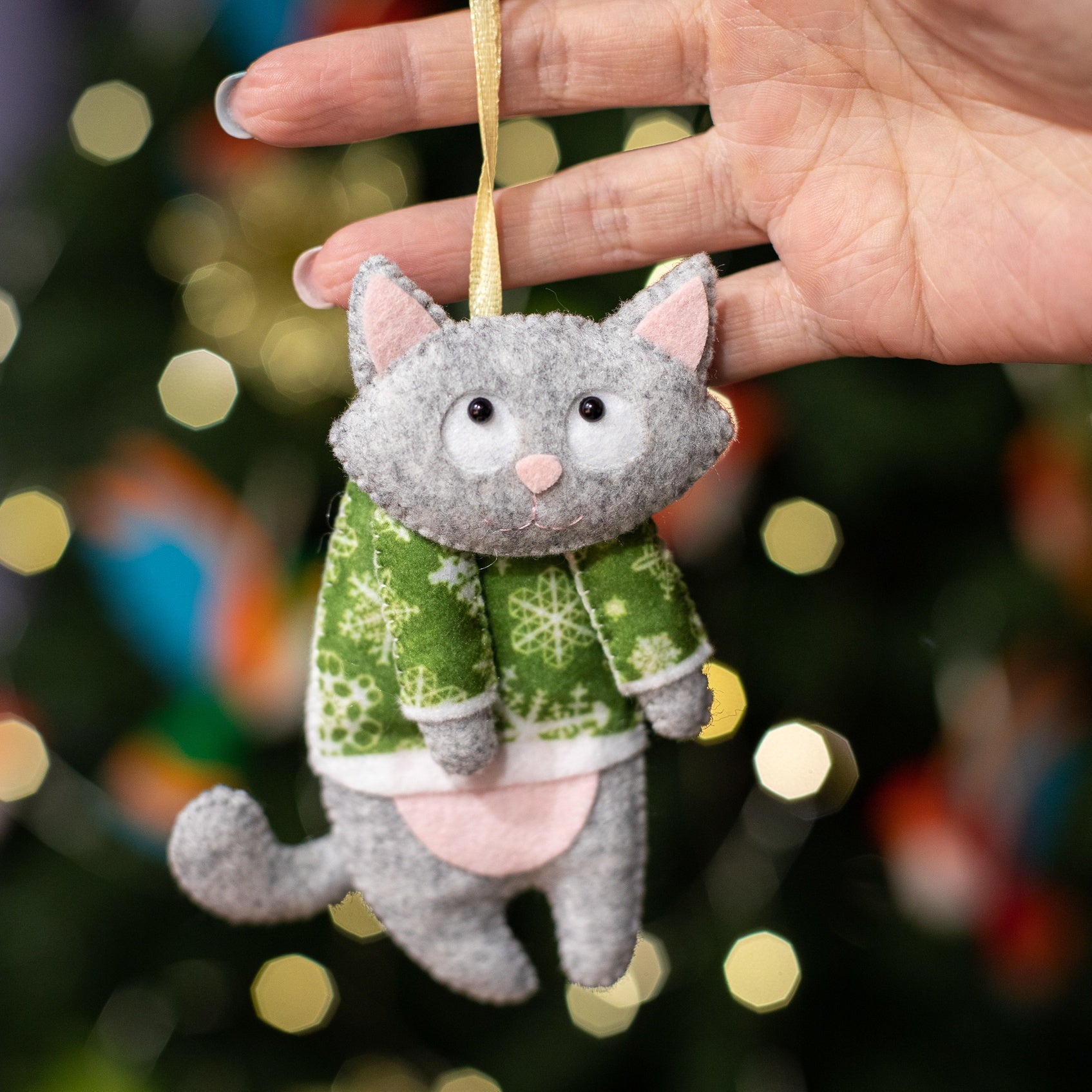 Felt cat ornaments wear in festive gray in a green sweater with snowflakes.