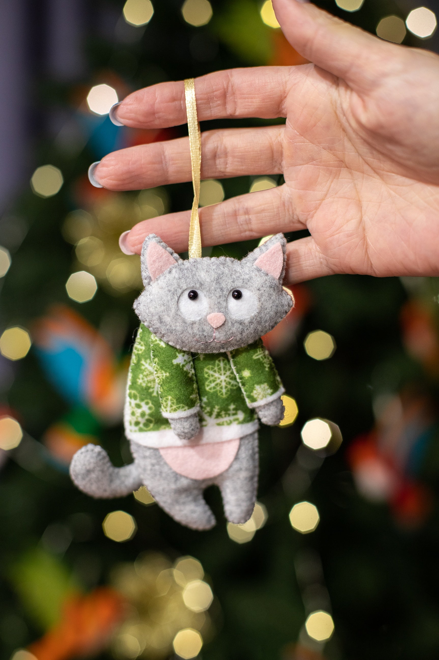 Felt cat ornaments wear in festive gray in a green sweater with snowflakes.