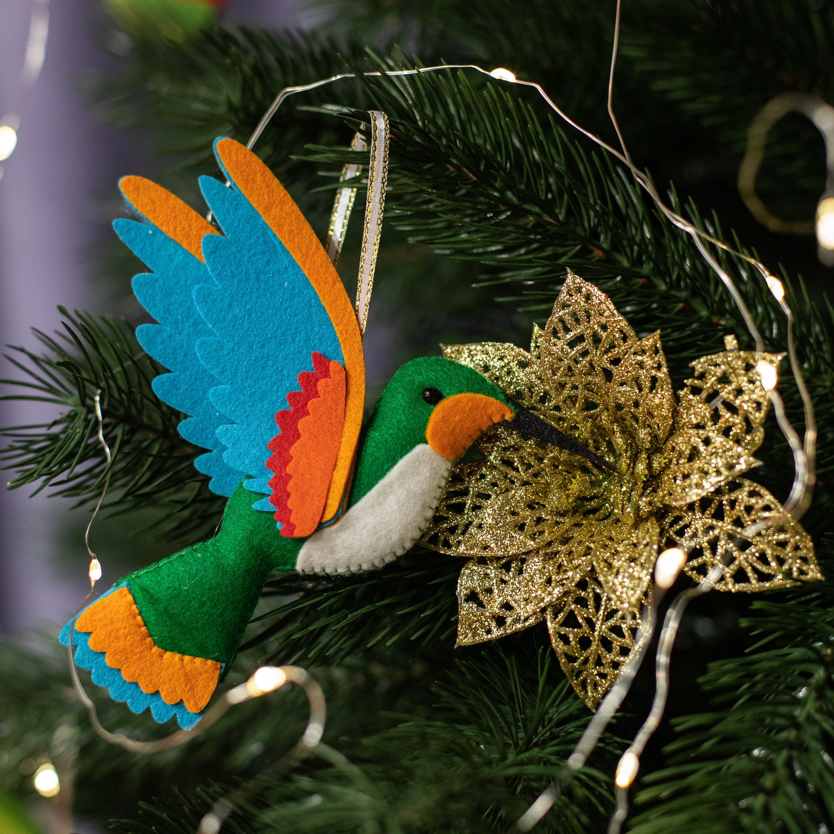 A handmade green felt hummingbird ornament with a white belly, blue wings, and a black beak