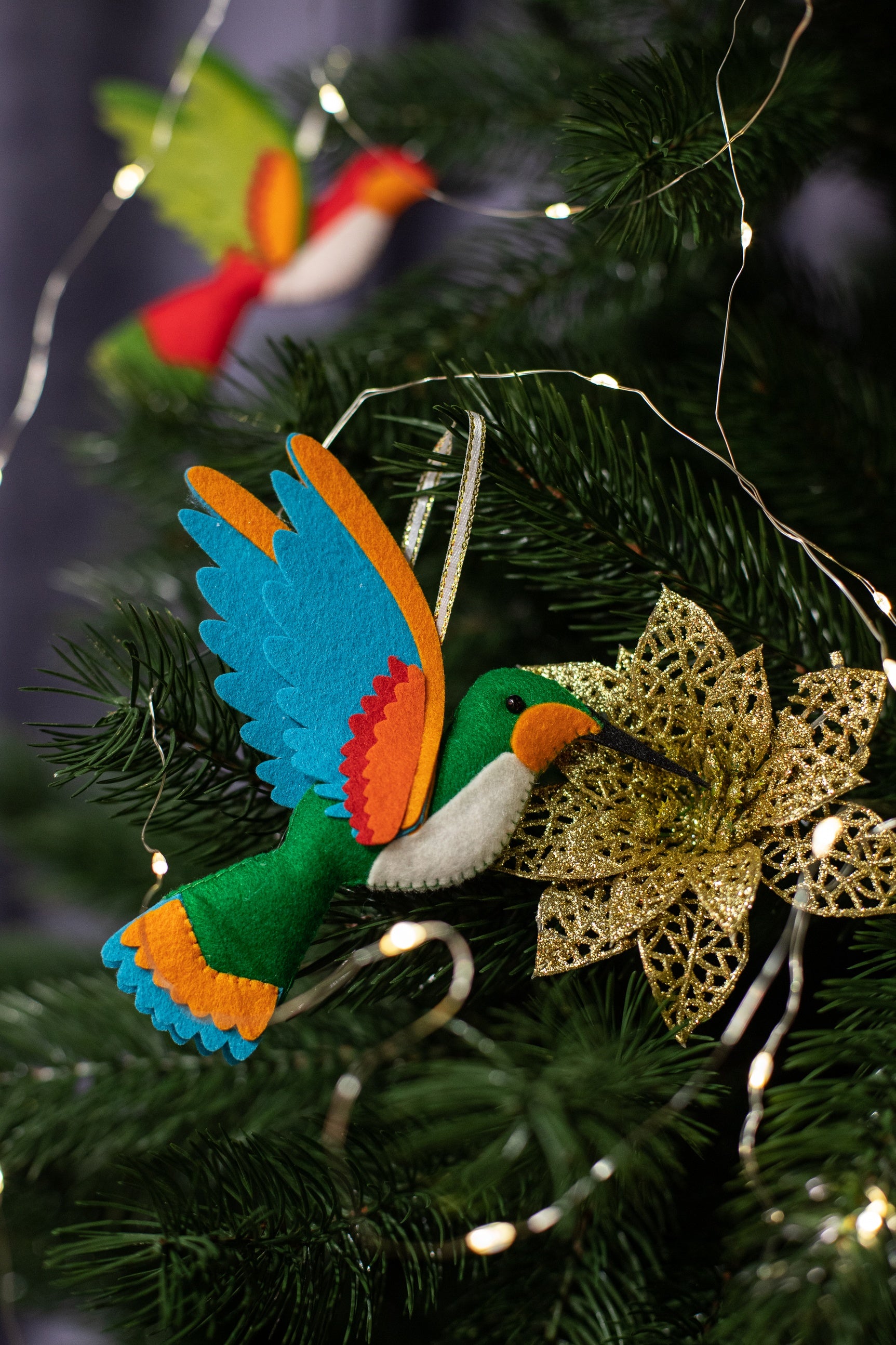 A handmade green felt hummingbird ornament with a white belly, blue wings, and a black beak