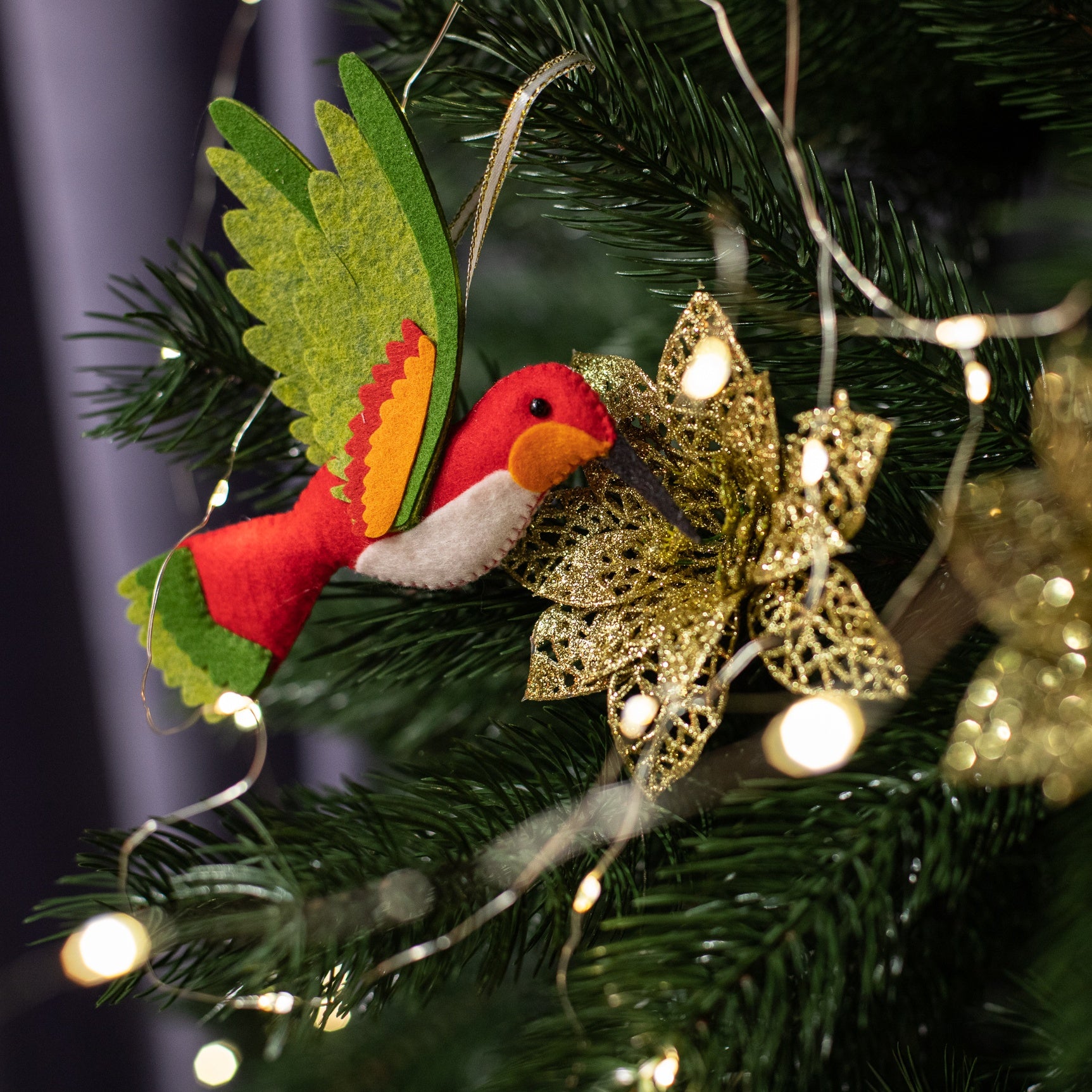A handmade red felt hummingbird ornament with a white belly, green wings, and a black beak