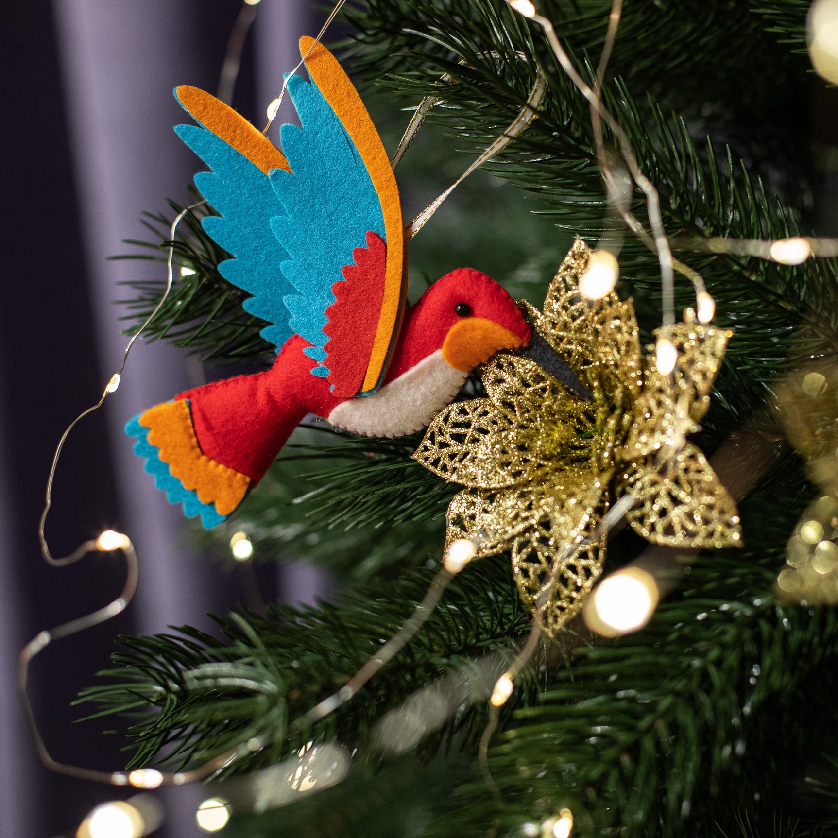A handmade red felt hummingbird ornament with a white belly, blue wings, and a black beak