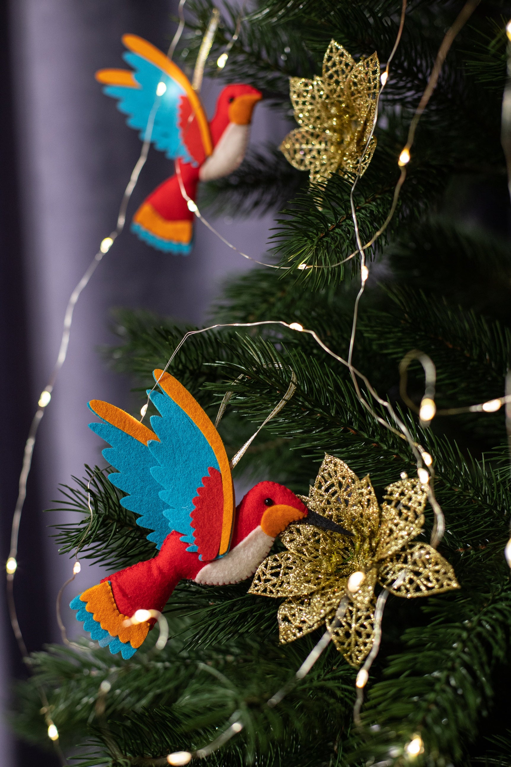 A handmade red felt hummingbird ornament with a white belly, blue wings, and a black beak