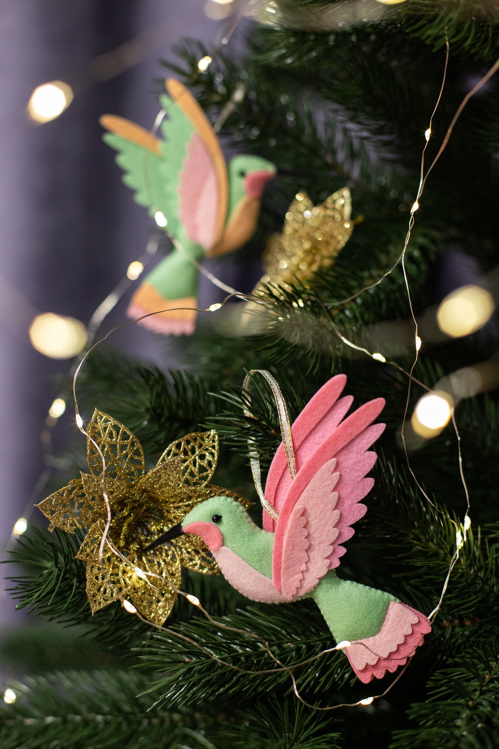 Handmade felt hummingbird ornament. The bird is mint green with a black beak. Its wings are a blend of peach and light pink. 