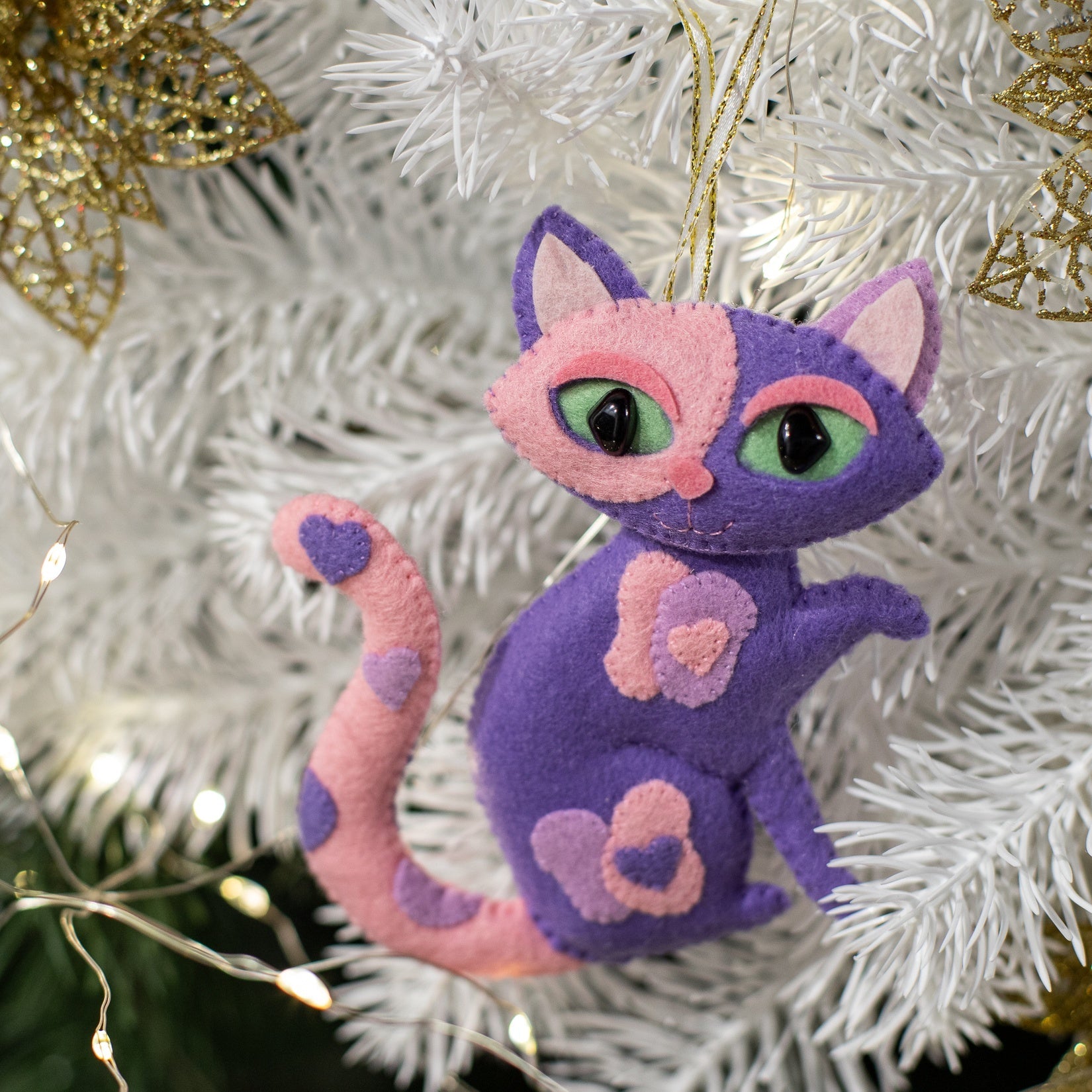 A purple and pink felt cat ornament with heart patches and a curled tail 