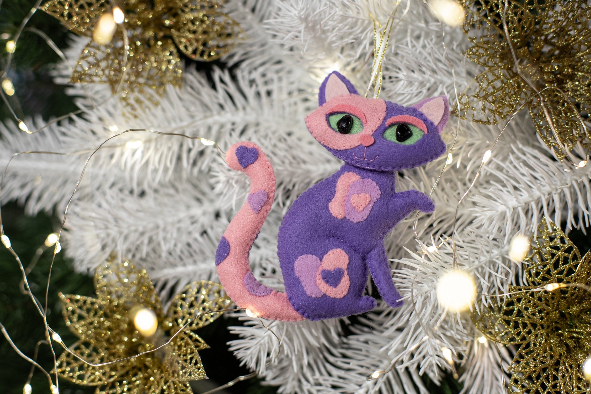 A purple and pink felt cat ornament with heart patches and a curled tail 