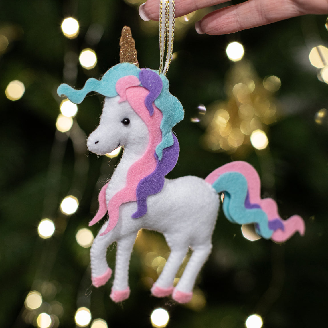 A handmade white felt unicorn ornament with a wavy pastel mane and tail in pink, purple, and teal, a sparkly gold horn, and pink hooves, with a gold loop for hanging.