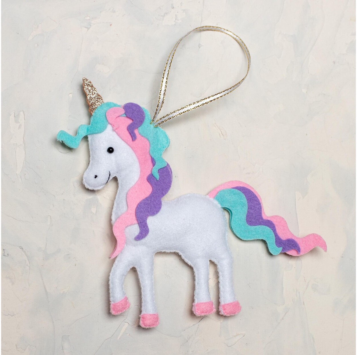 A handmade white felt unicorn ornament with a wavy pastel mane and tail in pink, purple, and teal, a sparkly gold horn, and pink hooves, with a gold loop for hanging.